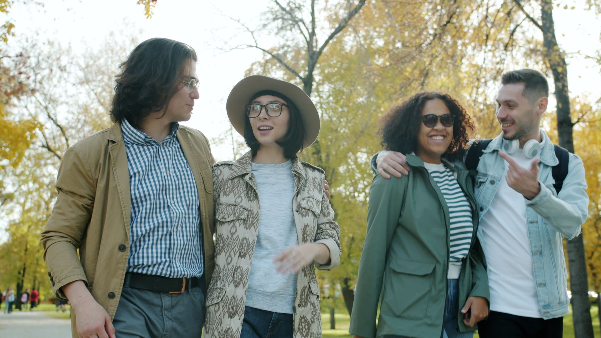 A diverse group of friends with arms around each other, laughing together in a sunny autumn park